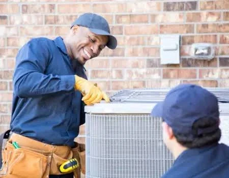 Two technicians working together on an outdoor air conditioning condenser